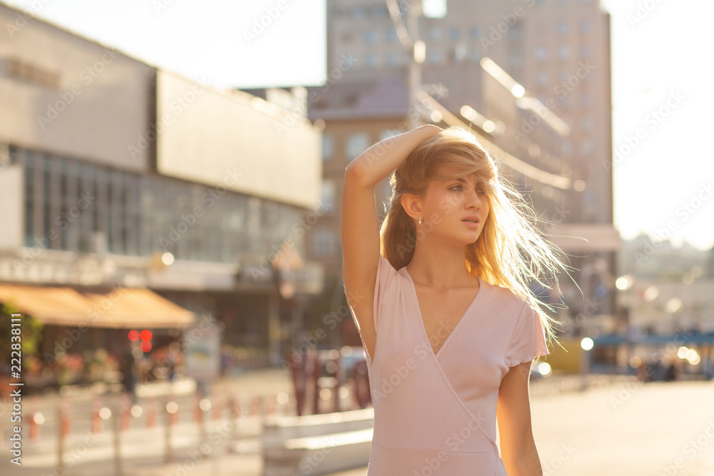Pretty blonde model posing at the street in a rays of sun. Lifestyle fashion concept. Space for text