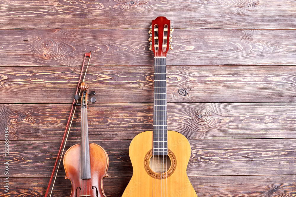 Naklejka premium Acoustic guitar and violin on wooden background. Vintage musical instruments on textured wooden surface with text space.