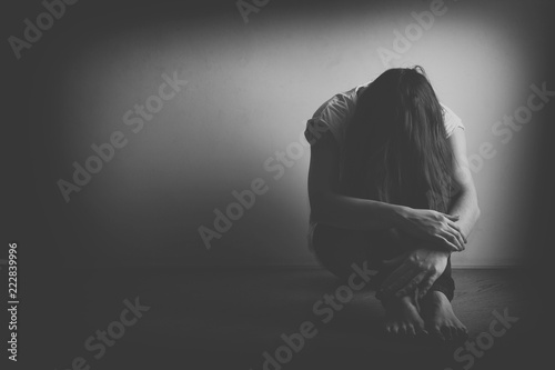 Teenager girl with depression sitting alone on the floor in the dark room. Black and white photo photo