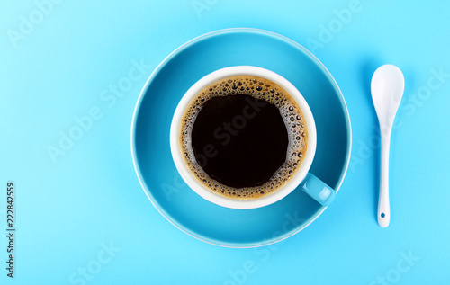 Full cup of black coffee and saucer over blue