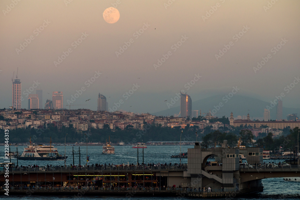 Evening view with the moon on the Bosporus Strait, the Galata Bridge and the Asian part of Istanbul. Selective focus.