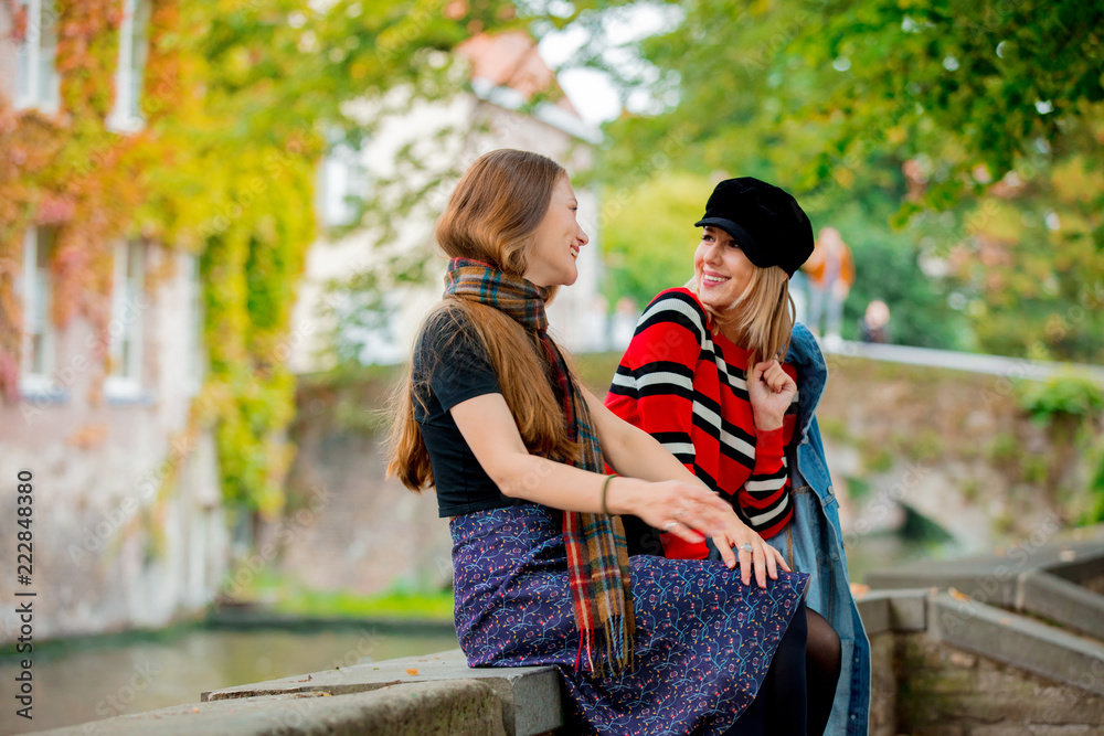 Fototapeta premium Young girlfriends talking on bridge in Bruges, Belgium. Autumn season