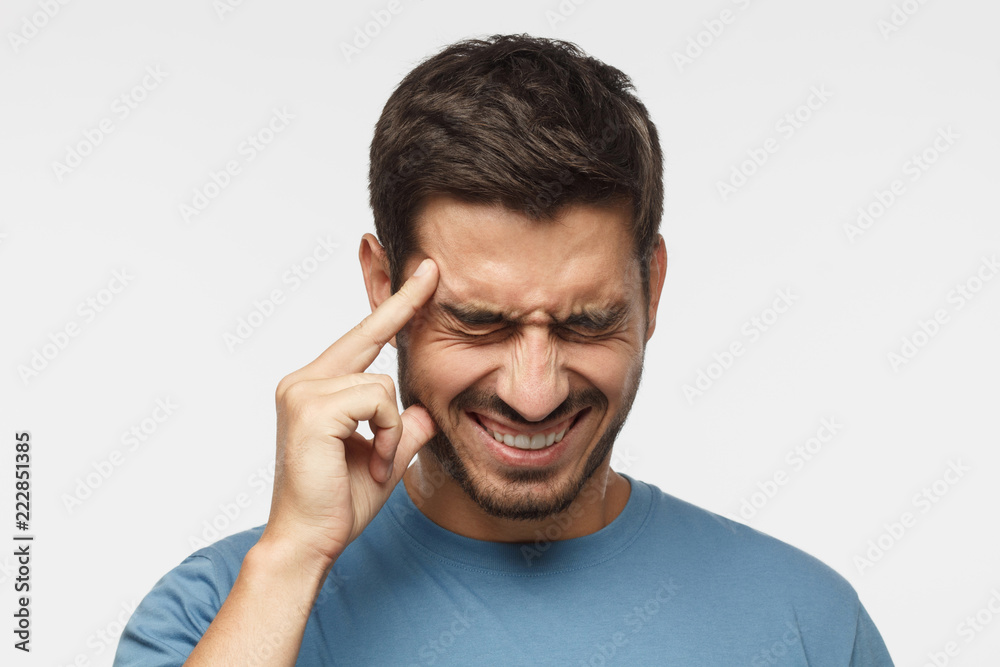 Headache concept. Young man isolated on gray background, showing how much his head hurts, experiencing pain, looking miserable and exhausted Headache concept. Young man isolated on gray background, showing how much his head hurts, experiencing pain, looking miserable and exhausted