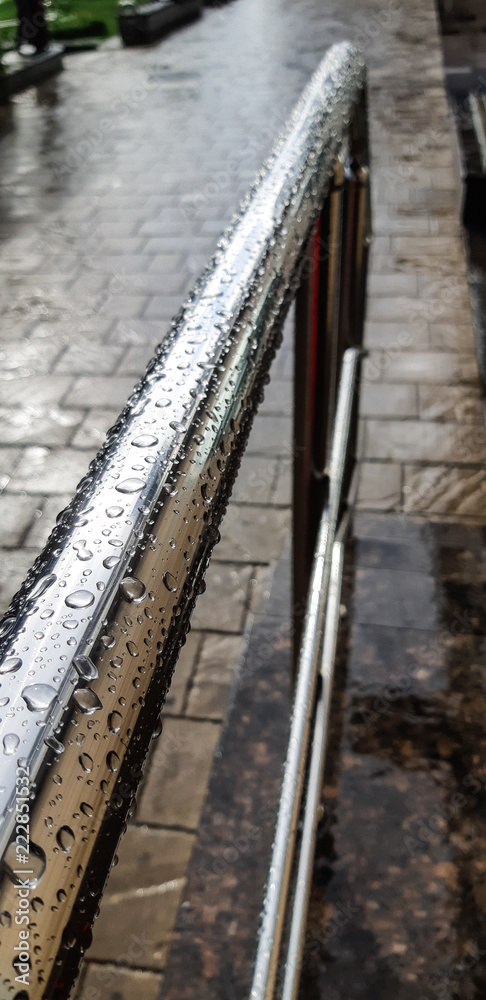 metal chrome-plated handrail in the drops of rain on a cobblestone sidewalk metal chrome-plated handrail in the drops of rain on a cobblestone sidewalk