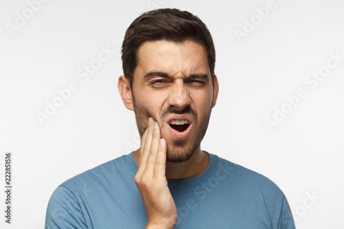 Obraz na plátně Closeup of young man isolated on gray background touching his face and closing e