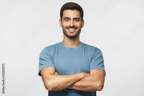 Smiling handsome man in blue t-shirt standing with crossed arms isolated on gray background photo