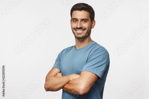 Portrait of attractive young sporty man in blue t-shirt standing with crossed arms isolated on gray background
