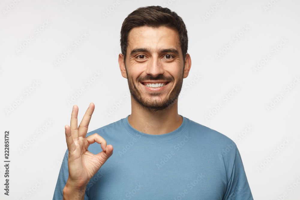 Young smiling man having happy look, gesturing, showing OK sign or showing okay gesture with his fingers Young smiling man having happy look, gesturing, showing OK sign or showing okay gesture with his fingers