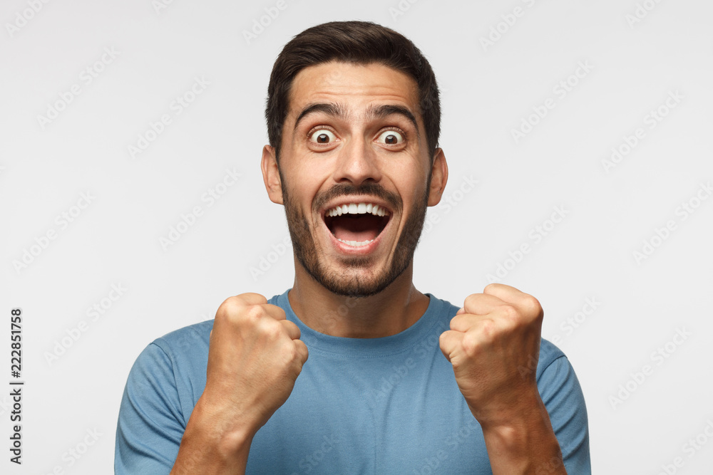 Young attractive man shouting while his team win, raised both fist in victory gesture, isolated on gray background. Soccer fan concept Young attractive man shouting while his team win, raised both fist in victory gesture, isolated on gray background. Soccer fan concept