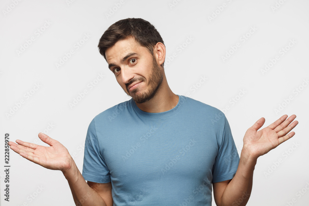 I don't know. Portrait of young confused man in blue t-shirt standing and shrugging shoulders, spreading hands isolated on gray background. I dunno I don't know. Portrait of young confused man in blue t-shirt standing and shrugging shoulders, spreading hands isolated on gray background. I dunno