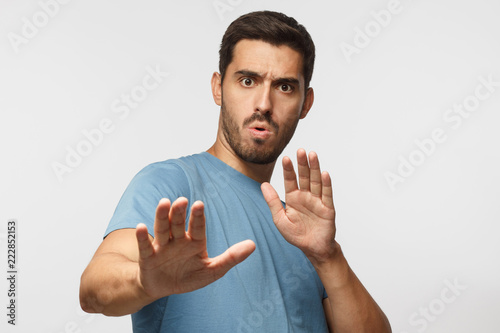 Young man showing stop gesture with both hands, wearin blue t-shirt, isolated on gray background photo