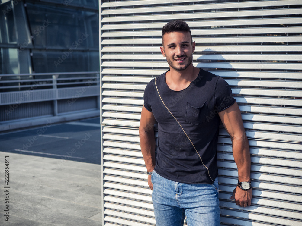 One handsome young man in urban setting in European city, wearing jeans and black t-shirt One handsome young man in urban setting in European city, wearing jeans and black t-shirt