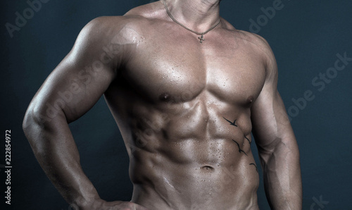 Torso of handsome  strong and sexy male fitness model bodybuilder poses on dark background
