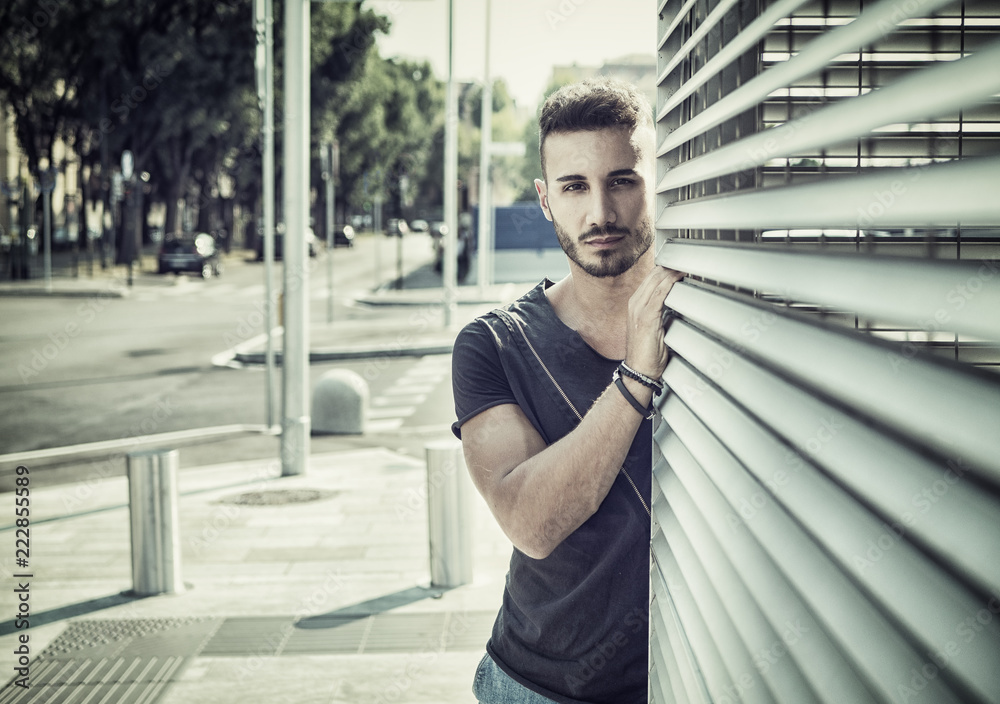 One handsome young man in urban setting in European city, wearing jeans and black t-shirt One handsome young man in urban setting in European city, wearing jeans and black t-shirt