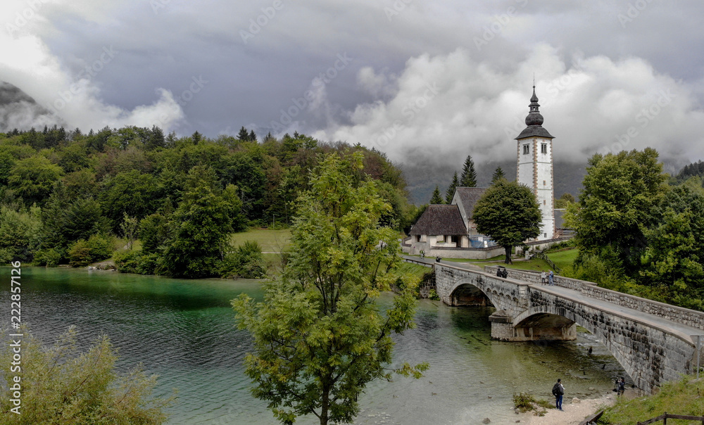 Church and bridge on Bohinj lake in slovenia. Very cloudy day