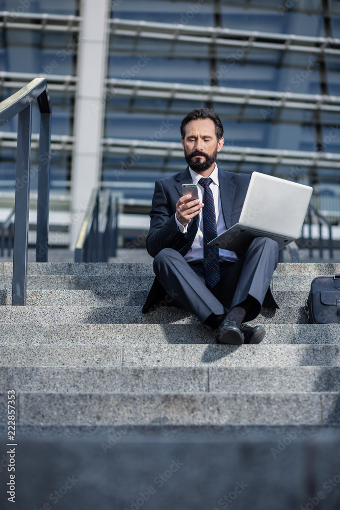 Serious businessman using his laptop on the stairs