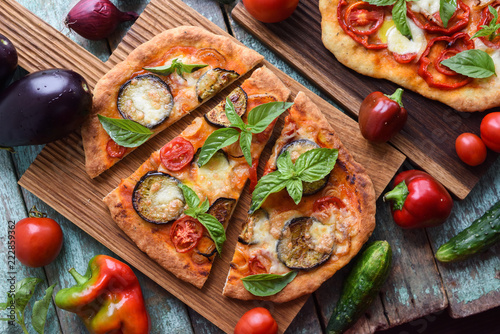 Healthy vegetarian pizza. Homemade rustic pizzas with egg plants, basil and tomatoes on oak boards served with raw ingredients