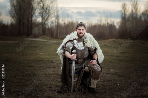 Quadro su tela Knight in armor with a sword in hand, standing on one knee.