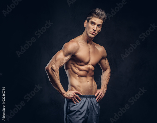Handsome shirtless ectomorph bodybuilder with stylish hair posing on a dark background. © Fxquadro