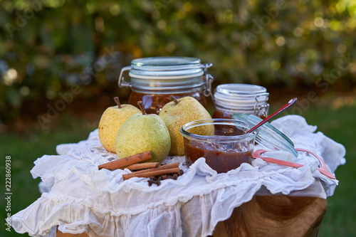 Close up Picture of homemade british, indian spicy pear chutney in small bowl with spoon and kidner jars, spice and pears on the small table with white rustic tablecloth photo