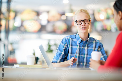 Young blonde confident woman explaining something to her colleague at working meeting in cafe