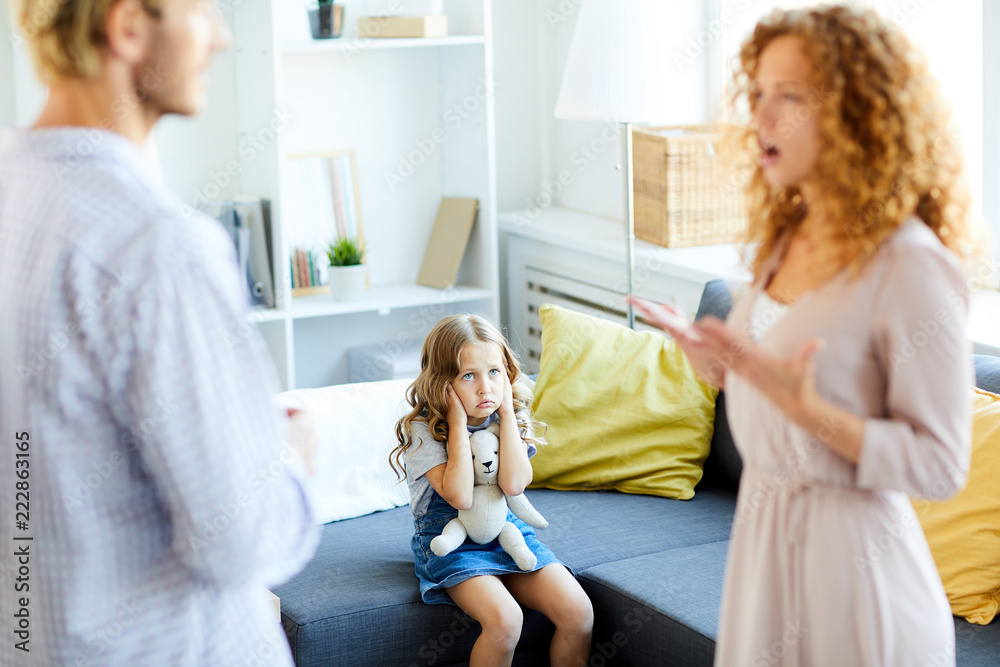 Shocked little daughter covering her ears while looking at her parents quarreling at home Shocked little daughter covering her ears while looking at her parents quarreling at home