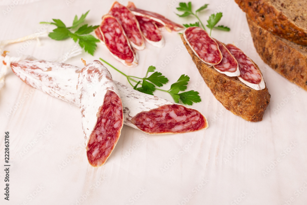 Salami and bread on white wooden background. Top view. Copy space