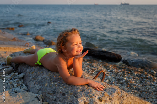 A little girl lies on a stone by the sea at sunset and dreams