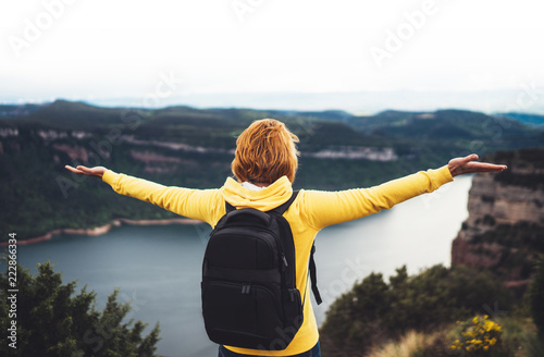 tourist traveler with backpack with raised hands on top on mountain, girl hiker view from back looking on mountain river with arms and enjoy nature panoramic landscape in trip, relax holiday concept