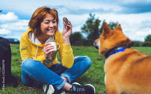 Happy girl with smile drink cup playing with red japanese dog shiba inu on green grass in the outdoors nature park  beautiful young woman hipster and dog friends  friendship lifestyle concept