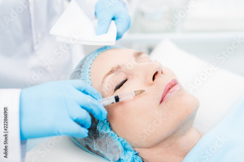 Cosmetician making rejuvenating injection between nose and upper lip of mature client