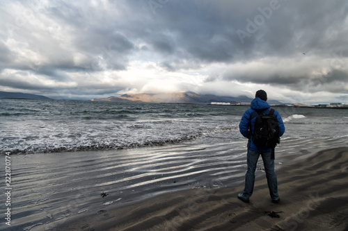 man looks on horizon with reykjavik seascape in iceland. future goals concept. nature lovers. travelling and wanderlust. man on sea shore look on seascape standing near water. dramatic sky in iceland