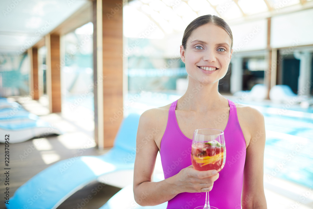 Young fit woman with glass of cocktail looking at camera with row of deckchairs on background Young fit woman with glass of cocktail looking at camera with row of deckchairs on background