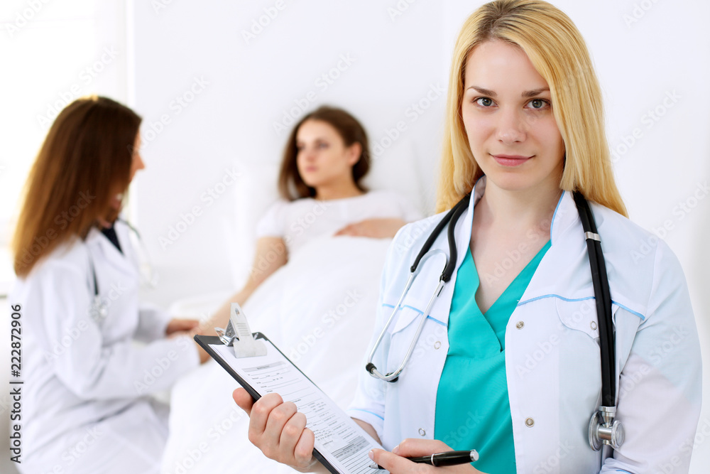 Doctor woman or nurse in a hospital office with her colleague and patient in the background. Healthcare and medicine concept Doctor woman or nurse in a hospital office with her colleague and patient in the background. Healthcare and medicine concept