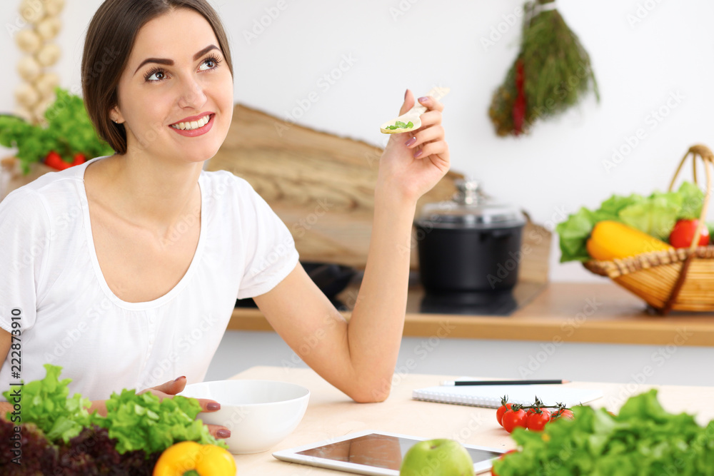 Beautiful Hispanic woman cooking in kitchen while using tablet computer and wooden spoon. Housewife found new recipe for dinner or breakfast. Healthy meal and householding concepts