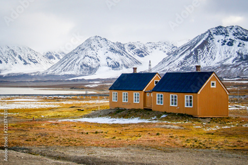 Yellow houses on yellow tundra grass with snowy mountains in the background, in Ny Alesund, Svalbard, Norwegian Arctic photo