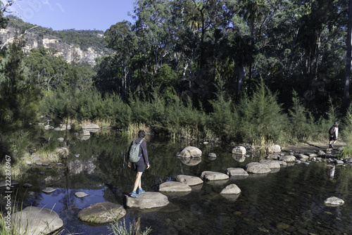 Female, baby boomer, hikers using stepping stones to cross the Carnarvon River in Carnarvon Gorge, Queensland, Australia.