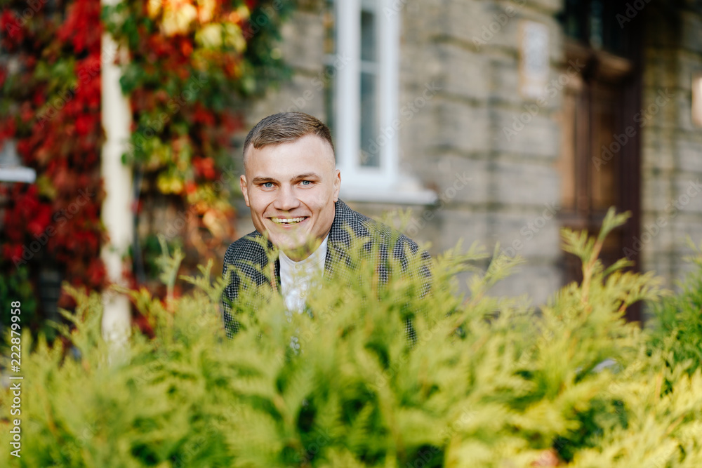 portrait of a stylish bridegroom with short hair against a background of a wall of autumn leaves portrait of a stylish bridegroom with short hair against a background of a wall of autumn leaves