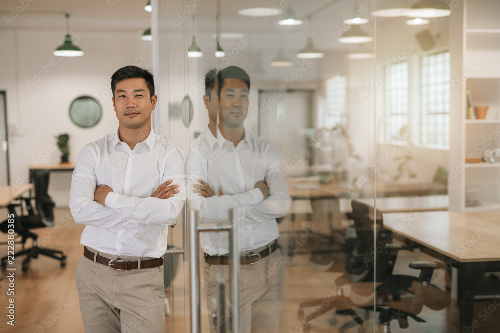 Asian businessman leaning against a glass wall in an office