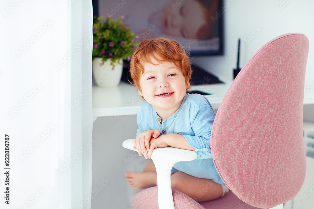 happy redhead toddler baby boy is sitting in office chair at working place happy redhead toddler baby boy is sitting in office chair at working place