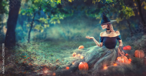 Fototapeta Halloween Witch with a carved pumpkin and magic lights in a dark forest at night