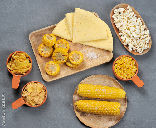 Corn set: boiled corn cobs with salt, corn slices cooked on the grill, flakes, tortillas, bowl with popcorn and canned corn kernels. Close-up. Gray background. View from above.