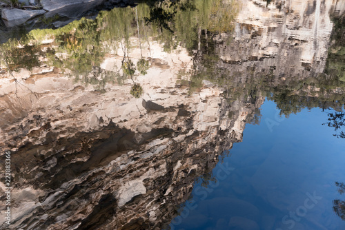 The sandstone walls of Carnarvon Gorge and the sky reflected in the calm water of the Carnarvon River on a sunny day, Queensland, Australia.