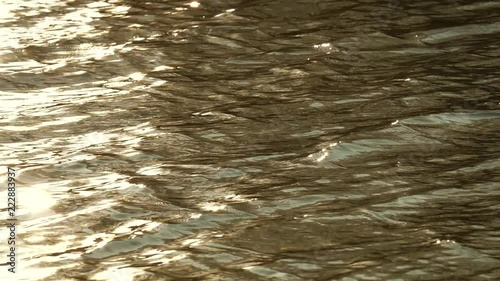 Slow motion of golden ripply water surface with waves at daytime photo