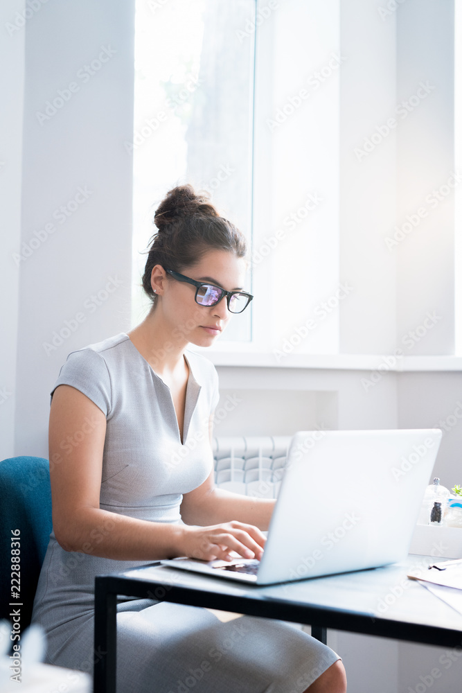 Portrait of beautiful young woman wearing glasses sitting alone at table in cafe and using laptop, copy space Portrait of beautiful young woman wearing glasses sitting alone at table in cafe and using laptop, copy space