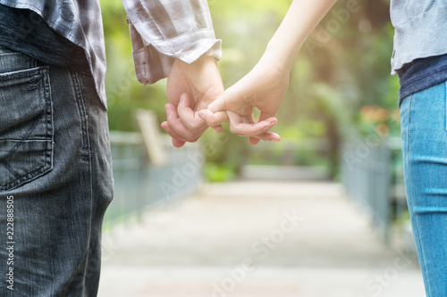 Love and friendship concept. Handsome man and young woman hold on to little fingers in public park background. Couple hands hook each other's little finger together.