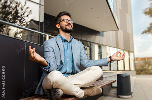 Businessman - mentally preparing for business meeting. Sitting in meditation pose in front of office building and smiling  