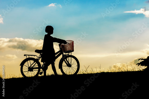 silhouette cute little girl riding bike in park at sunset background