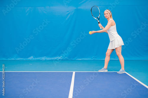 Full length  portrait of female tennis player serving ball and holding racket in indoor court, copy space © Seventyfour