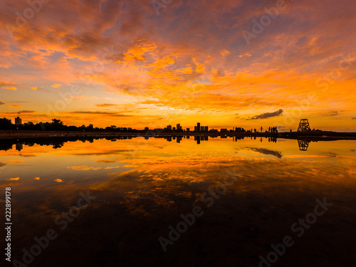 Beautiful, bright, saturated, and vivid sunset with colorful orange, yellow, blue, pink and purple clouds in the sky above reflecting on rain puddles in the sand at Montrose Beach in Chicago Illinois.